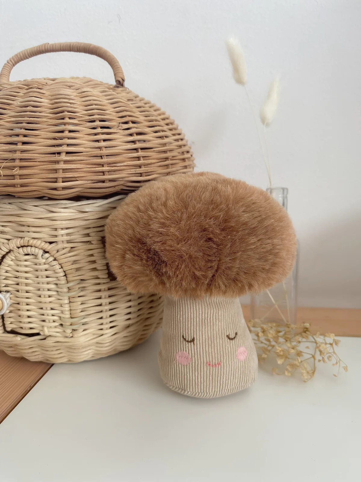 Stuffed mushroom toy with a brown, fuzzy cap and tan, corduroy stem featuring a smiling face, next to a stacked set of wicker baskets.