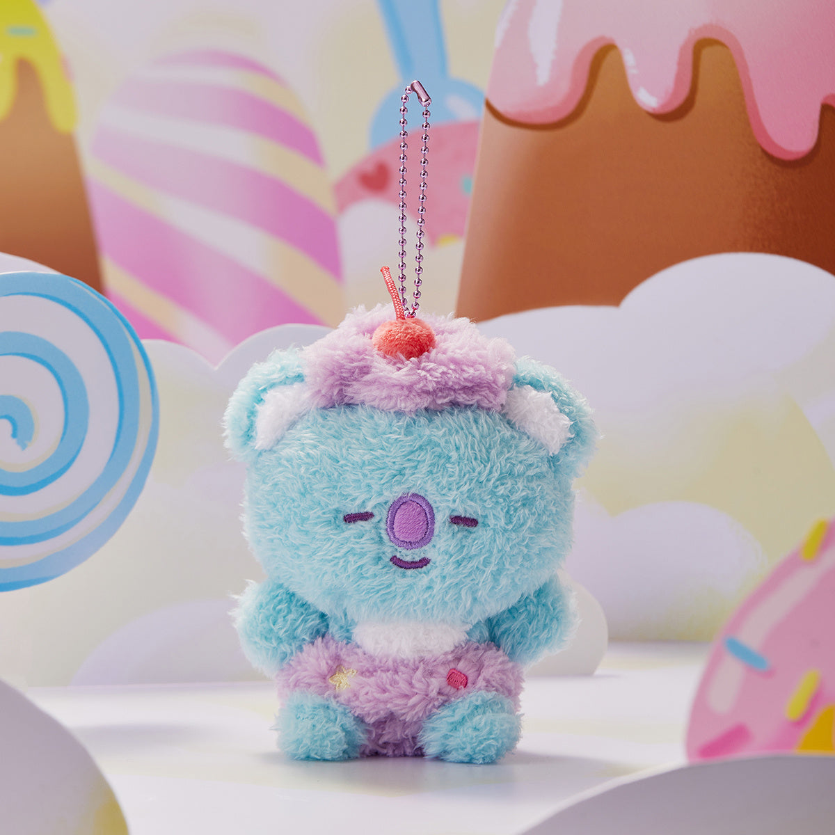 Blue plush koala with cupcake hat in a candy landscape.