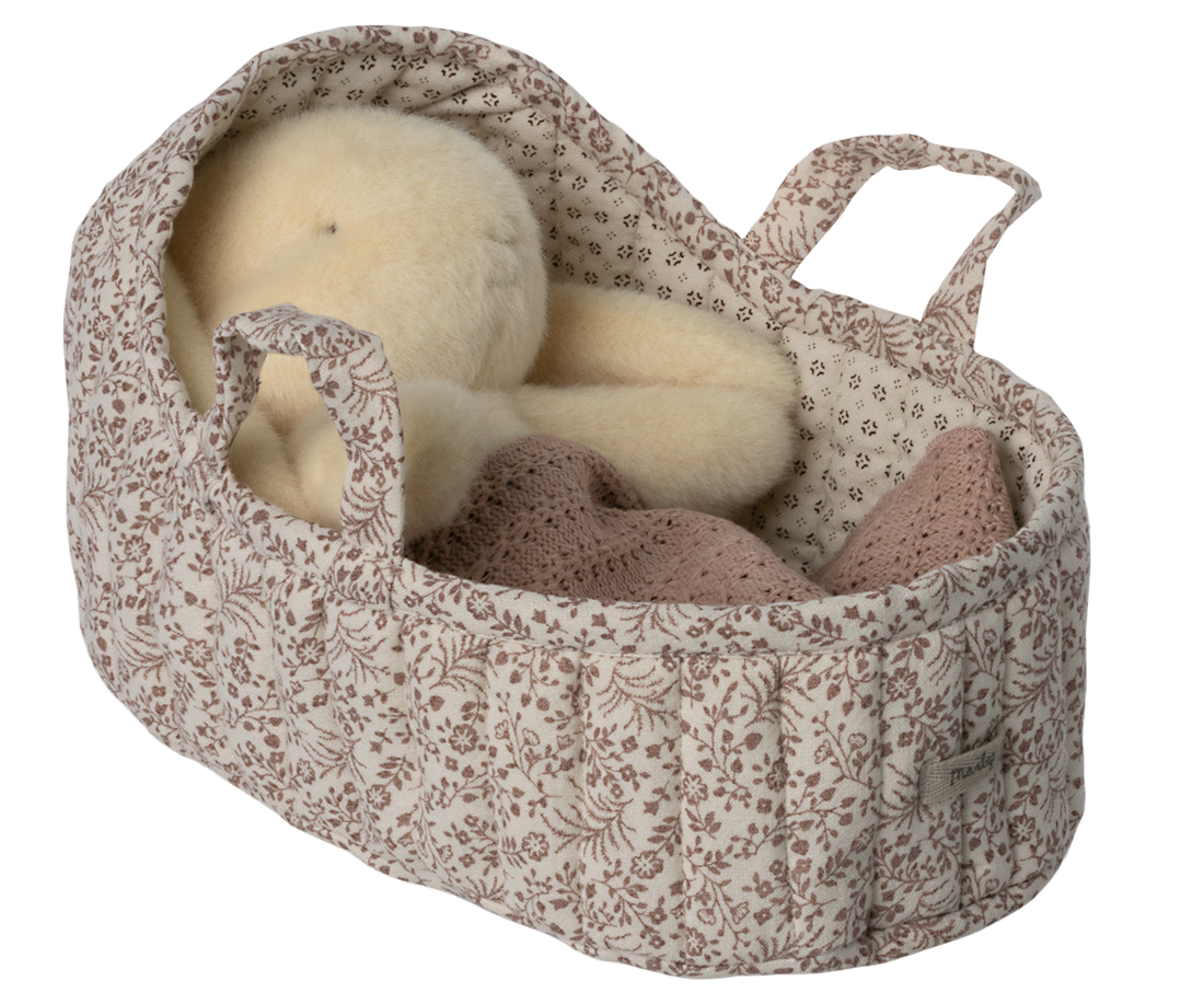Stuffed animal in floral bassinet with knit blanket.
