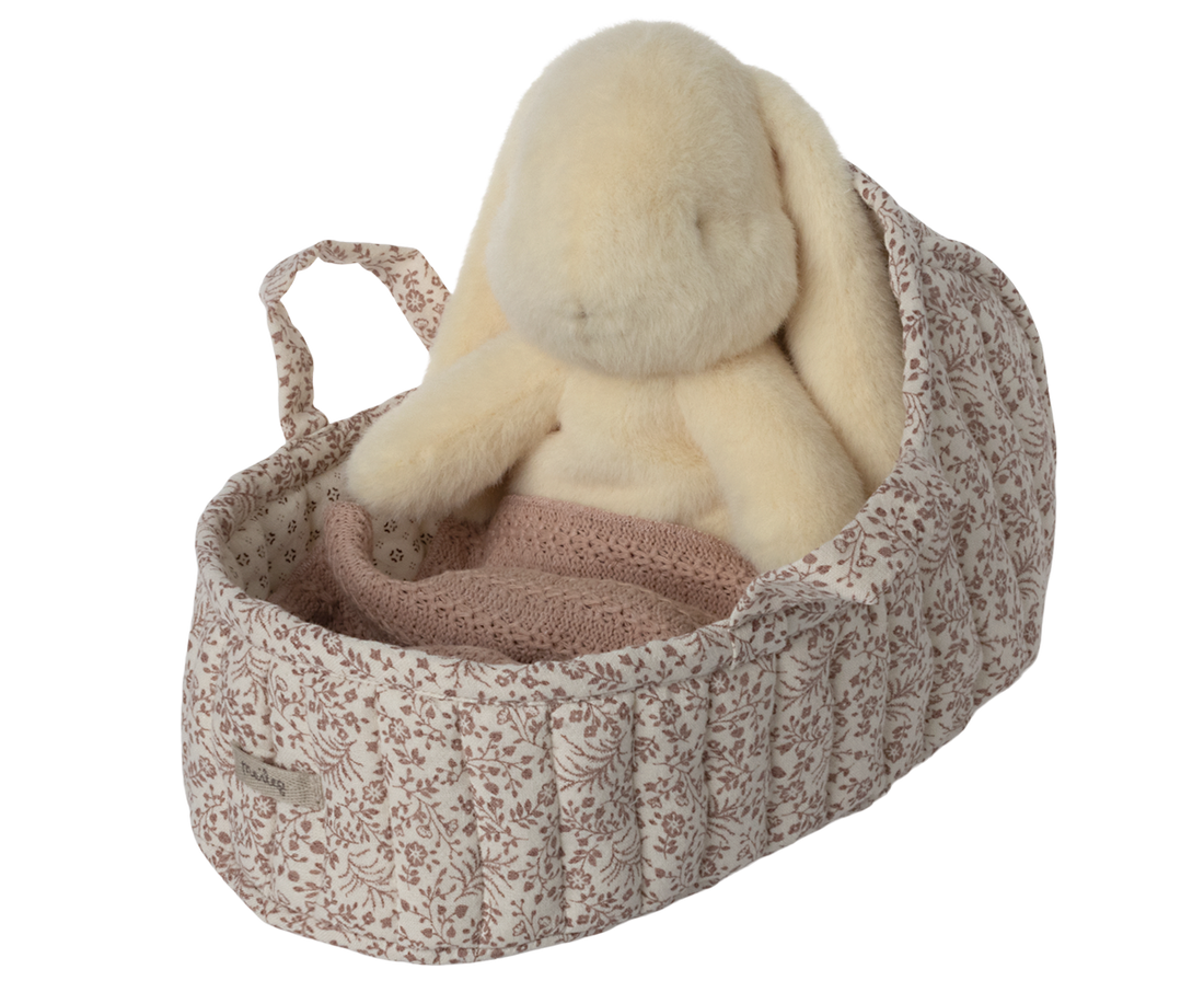Stuffed bunny in floral-print fabric bassinet with pink knit blanket.