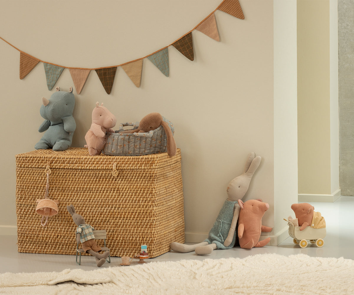 A room scene of stuffed animals with bunting, including a rhino, hippo, and rabbits, arranged on and around a wicker chest and baby carriage.