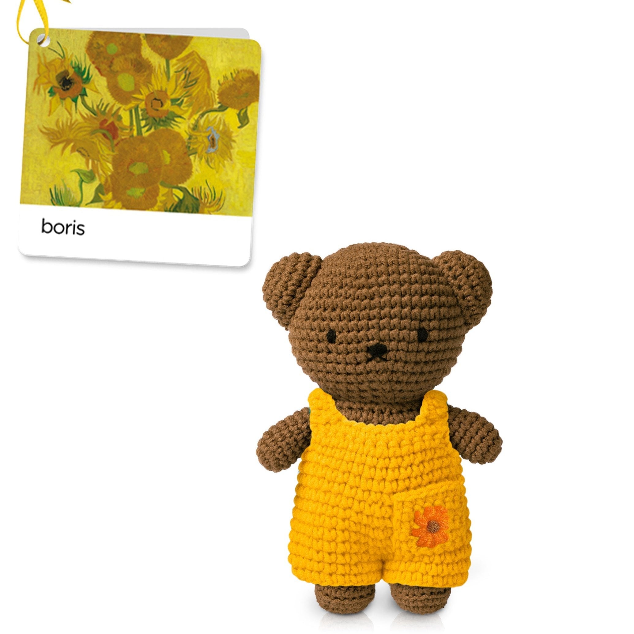 Crocheted brown bear toy wearing yellow overalls with a flower accent.