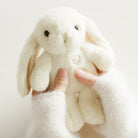 Off-white stuffed bunny held in hands wearing off-white wool sweater.