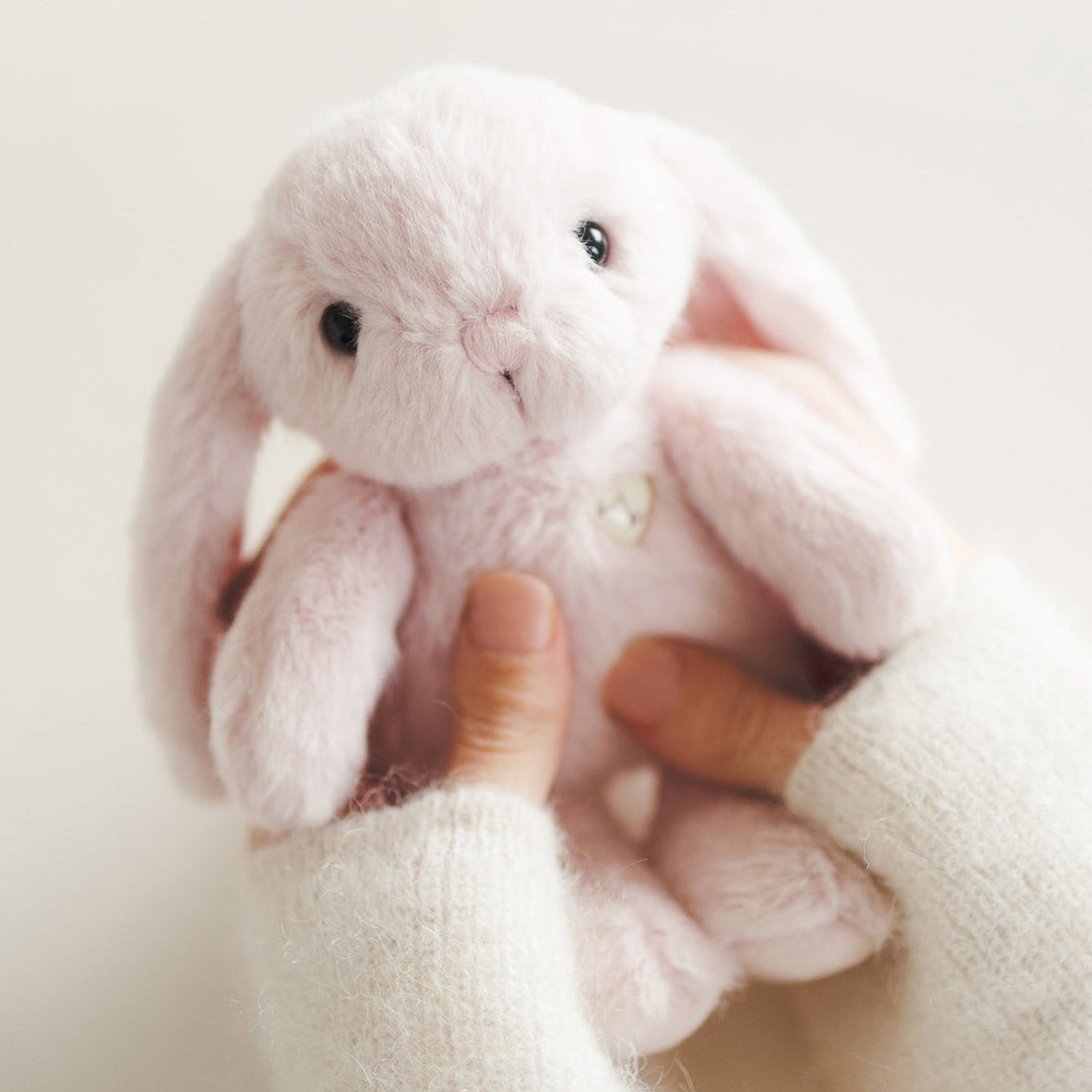 A person holding a plush pink bunny while wearing fuzzy white sweater sleeves.