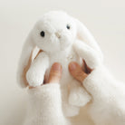 Close-up of a white stuffed bunny held by hands in off-white knit sleeves.