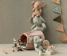 Stuffed elephants stacked next to a polka-dot toy tunnel with toy mice, a toy campfire, and a toy tea set with macarons. There is also a banner of triangular flags.