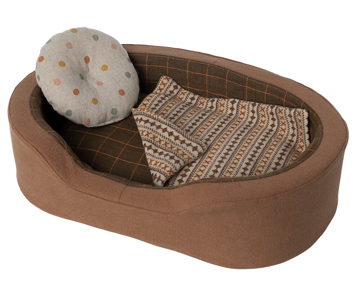 Brown dog bed with a polka dot pillow and patterned blanket.