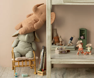 Here are some descriptive alt tags for the image:
*   **Stacked plush toys: brown bear leaning on a seated gray bunny on a rattan chair.**
*   **Playroom scene: assorted stuffed animals and miniature furniture against a pastel background.**
*   **Display of children's toys: Maileg mice on scooter and bicycle, plush rabbits and bears.**
*   **Close-up of toy arrangement: rattan chair, wooden shelves with plush animals, vintage vibe.**