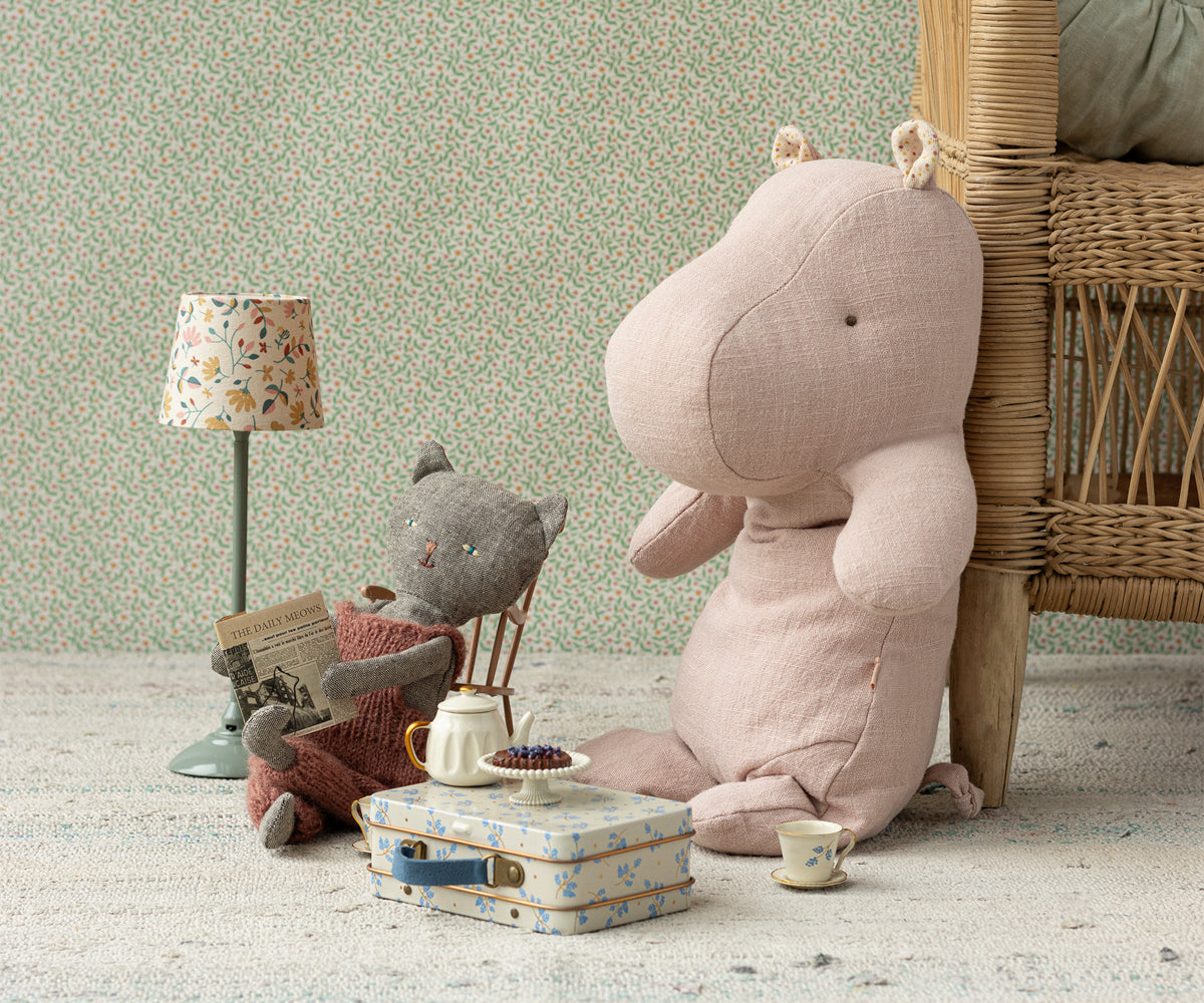 Stuffed cat doll reading newspaper, hippo plush toy, miniature tea set, floral suitcase, floor lamp.