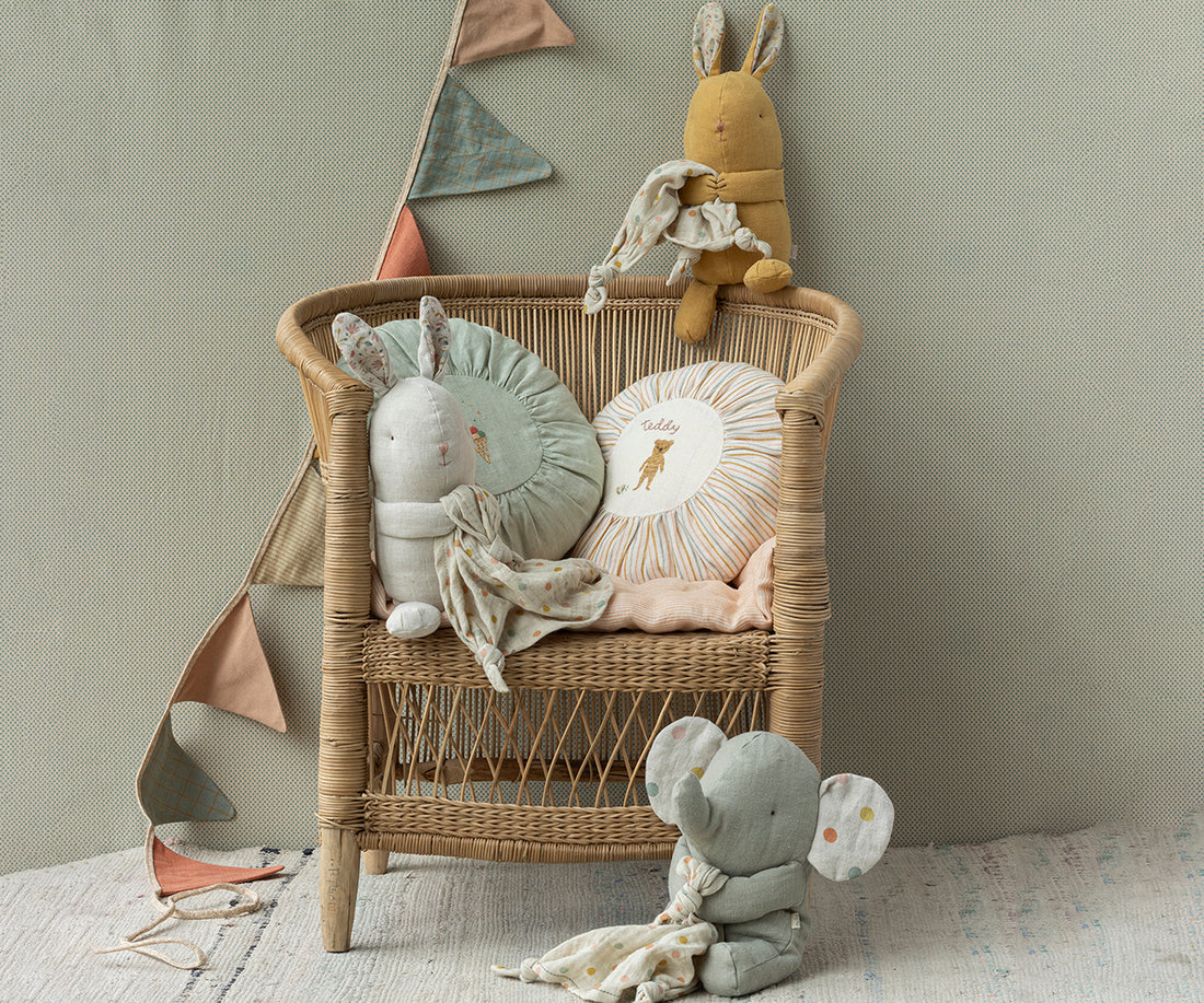 Wicker chair with stuffed animals and pillows, bunting in the background.