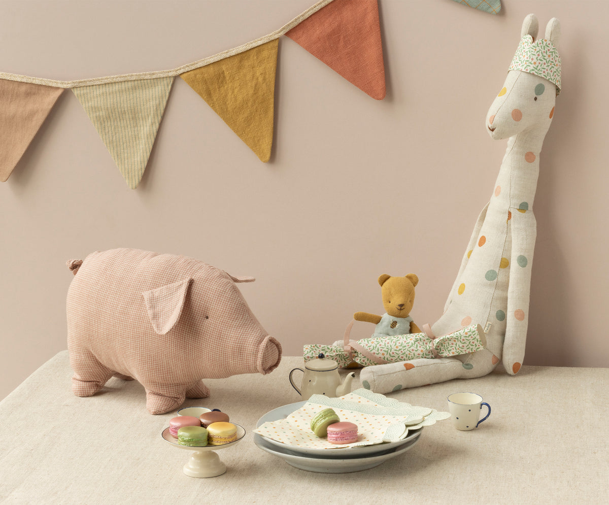 Stuffed giraffe, pig, and bear toys with macarons on a table in front of a pink wall.