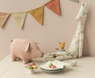 Stuffed giraffe, pig, and bear toys with macarons on a table in front of a pink wall.