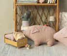 Still life with plush pig pillows, toy bed, rattan shelf, and stuffed rhino in mug.