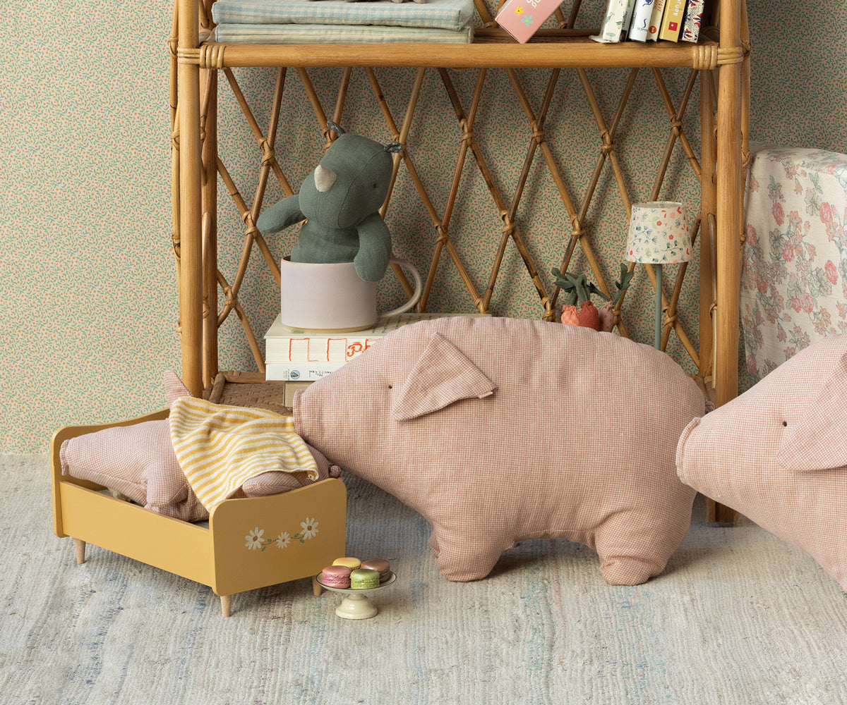 Still life of a child's room with pig pillows, a yellow doll bed, and a stuffed rhino on a bookshelf.