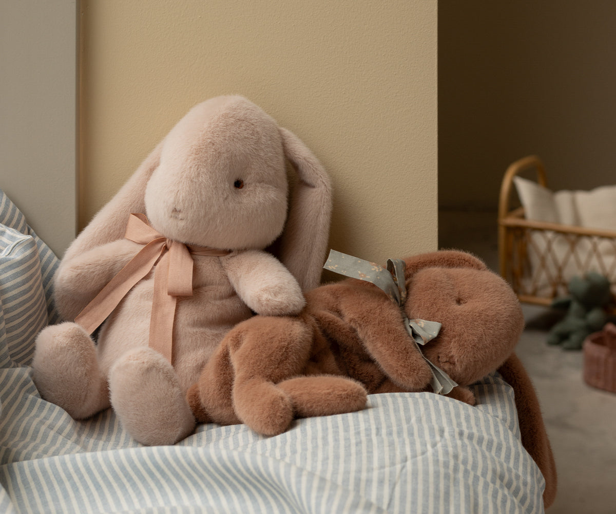 Two plush bunny toys, one pink and one brown, sitting on a striped blue and white cushion.