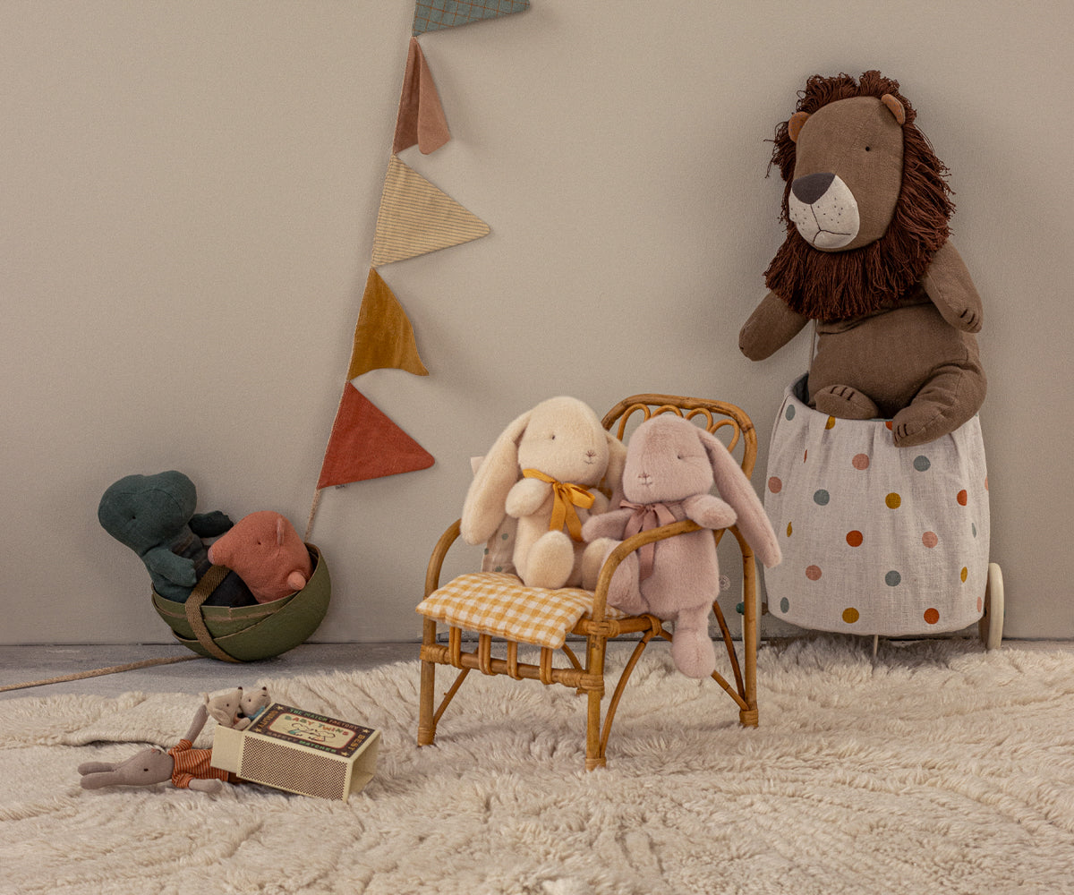 Product shot of stuffed animal toys on a wicker chair and floor.