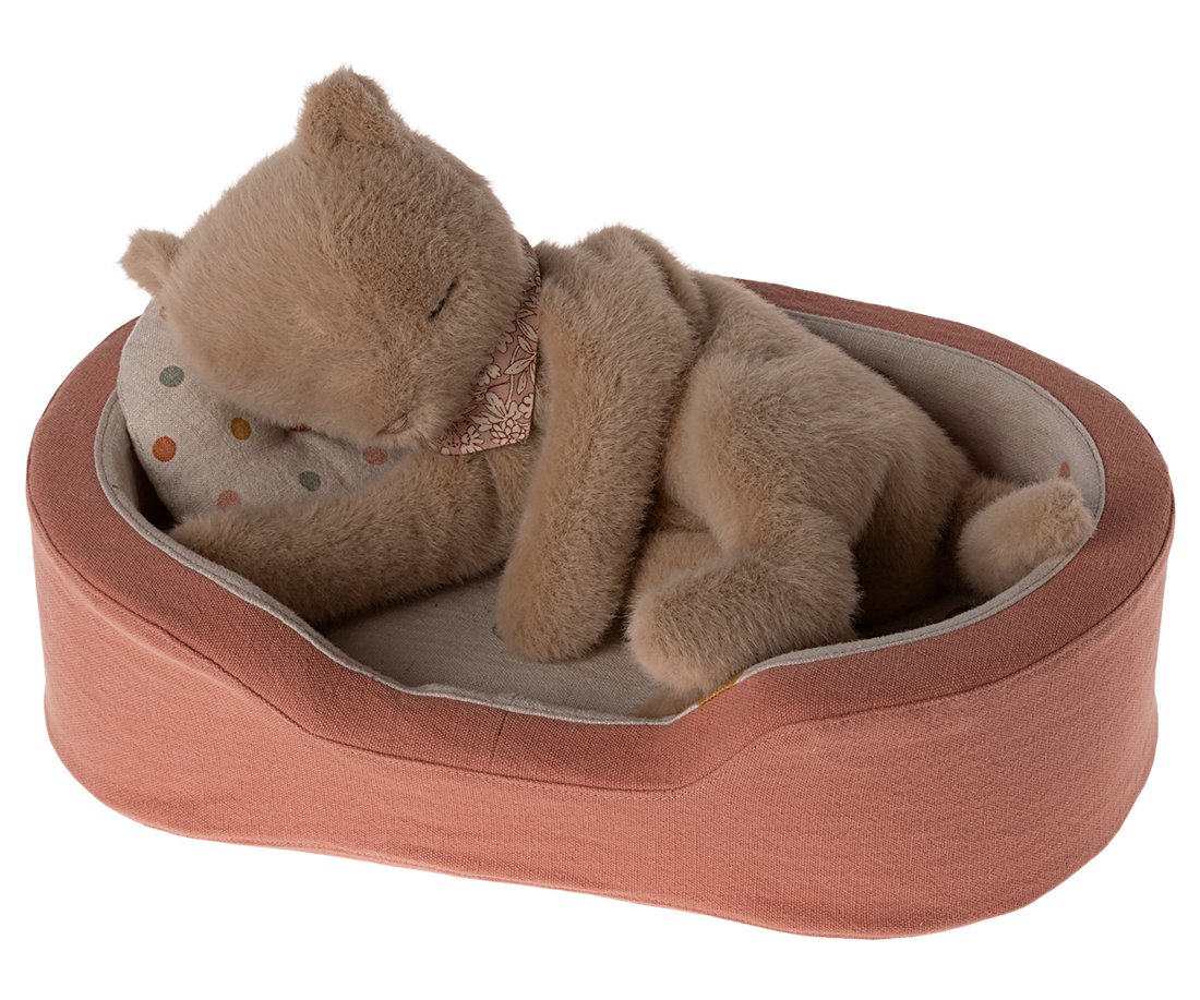 Tan, plush cat toy sleeping in a salmon-colored pet bed with a patterned pillow.