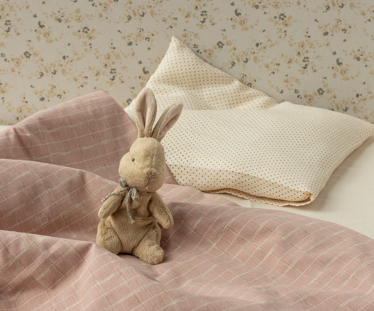 Stuffed bunny on a pink and white checkered blanket with patterned pillows in the background.