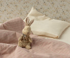 Stuffed bunny on a pink and white checkered blanket with patterned pillows in the background.