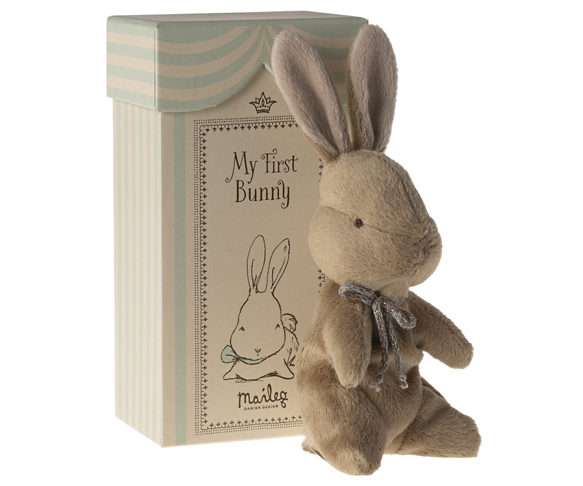 Stuffed brown bunny with gray ribbon next to patterned box.