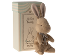 Stuffed brown bunny with gray ribbon next to patterned box.