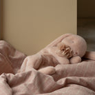 Pink plush bunny with flower resting on a pink and white checkered blanket.