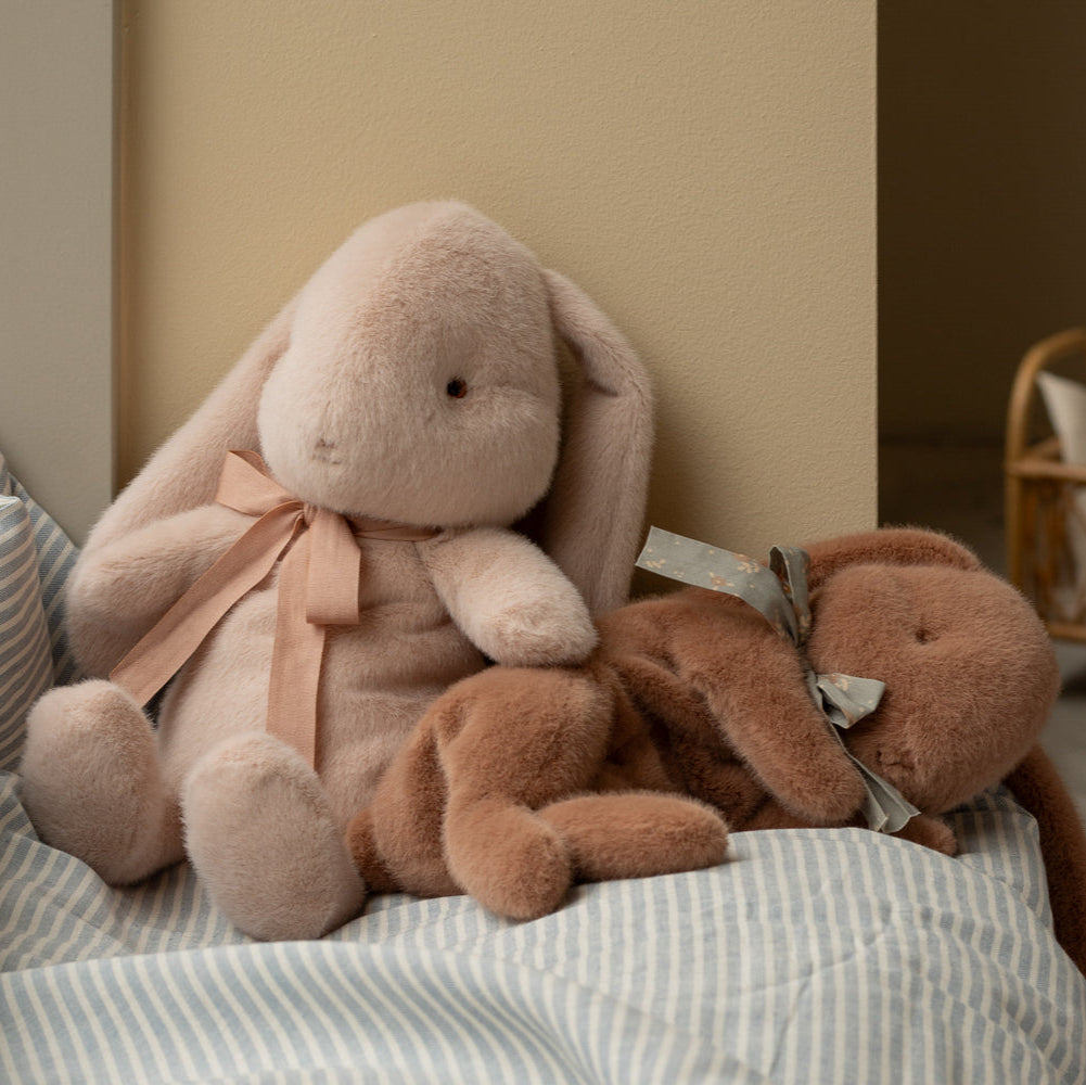 Two plush bunny toys with ribbons on a striped fabric surface.