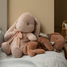 Two plush bunny toys with ribbons on a striped fabric surface.