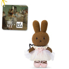 Crocheted brown bunny ballerina in a white dress with pink details, featuring a tag with art and brand logos.