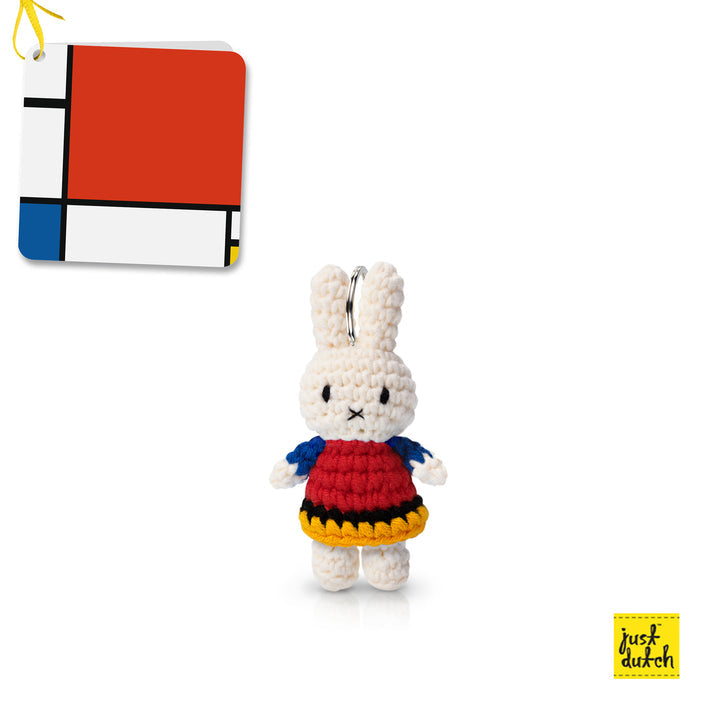 Crocheted Miffy doll keychain, red dress with yellow and black trim, blue sleeves. Mondrian-inspired tag.