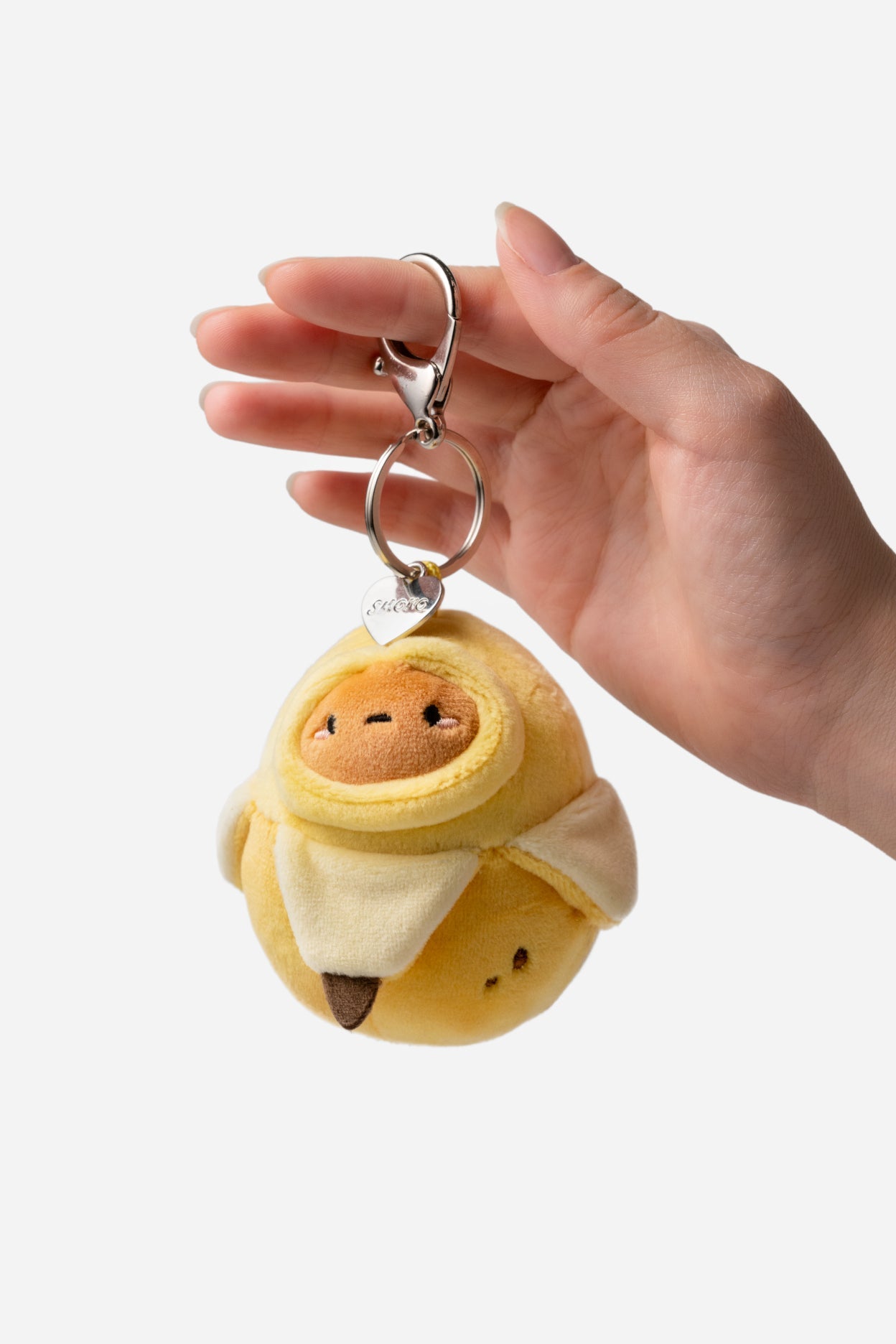 Plush keychain shaped like a cartoon character held by a hand against a white background