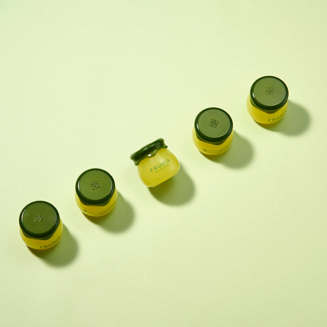 Five small yellow Frudia jars with dark green lids arranged diagonally on a light green background.