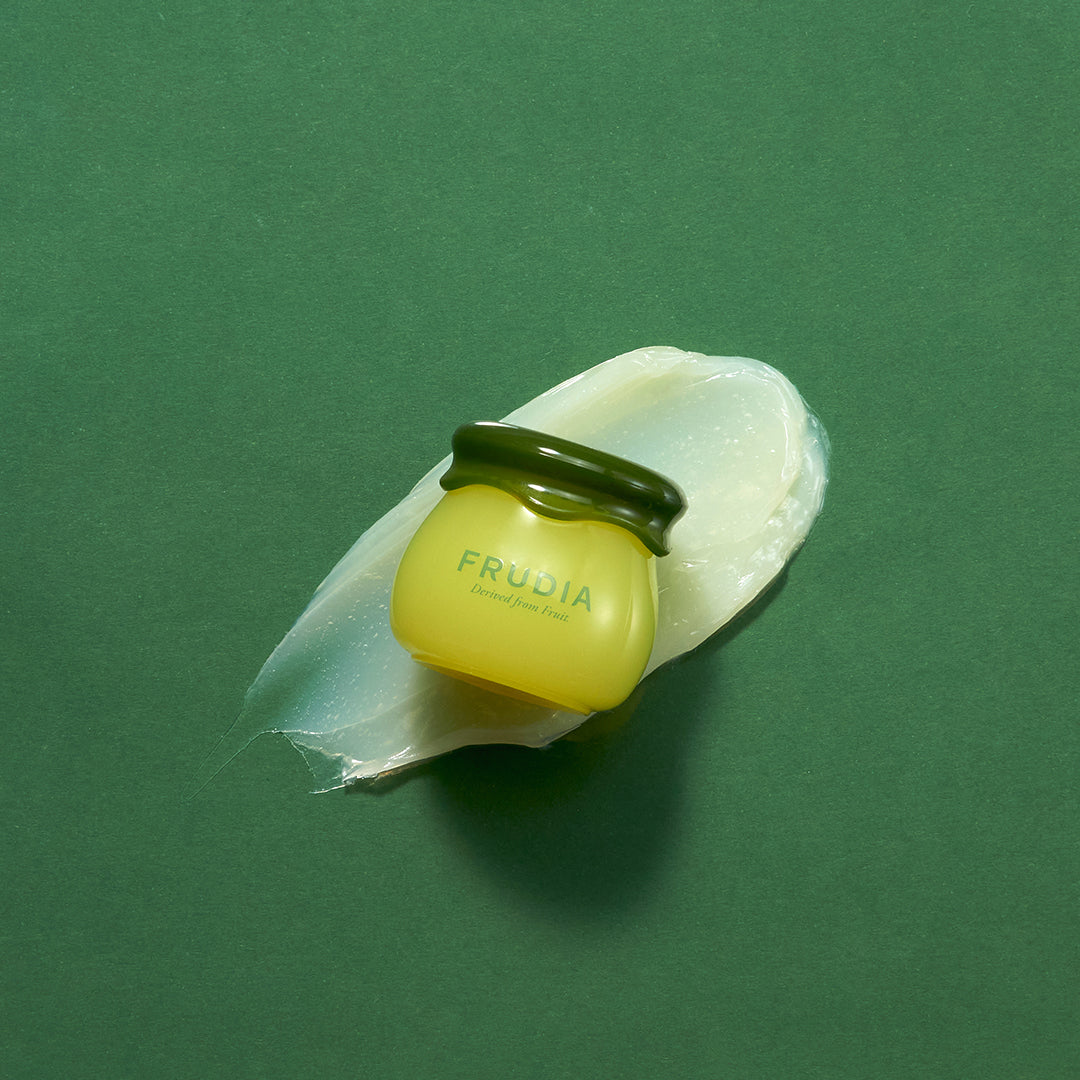 A jar of Frudia skin cream on a swatch of product against a dark green background.