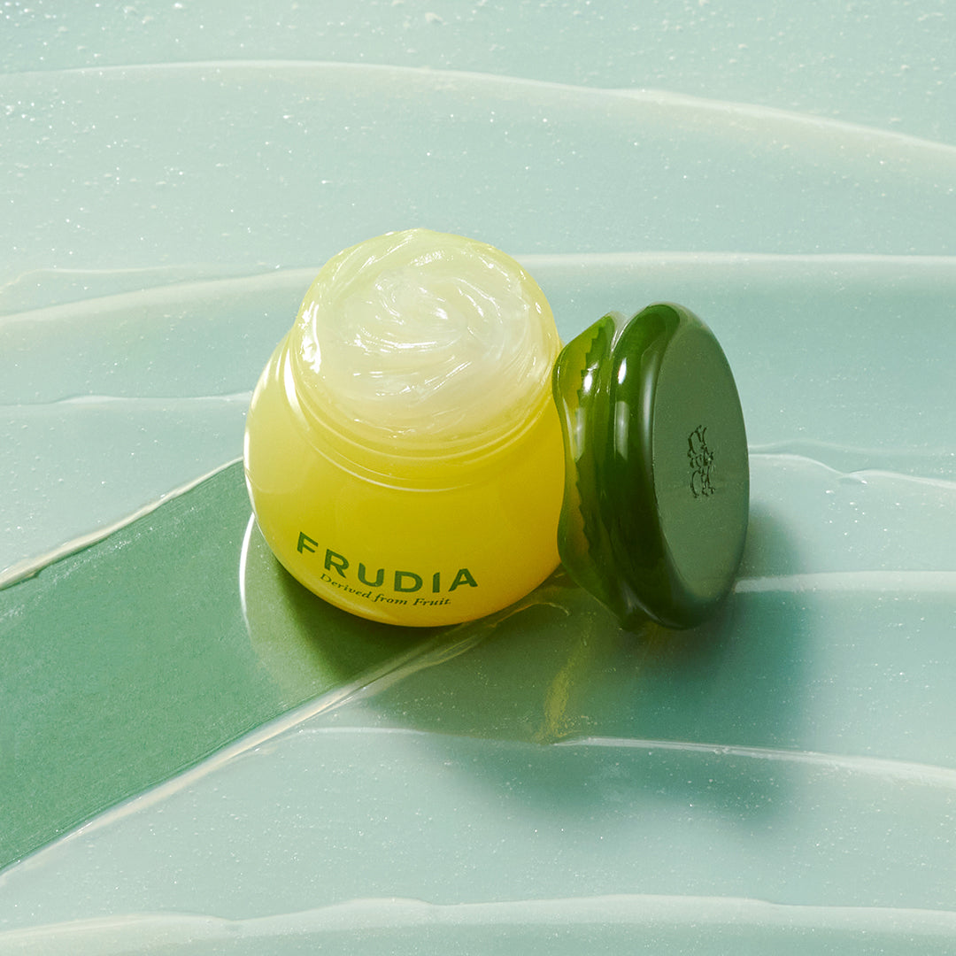 Yellow frudia cream with green lid on top of minty blue backdrop.