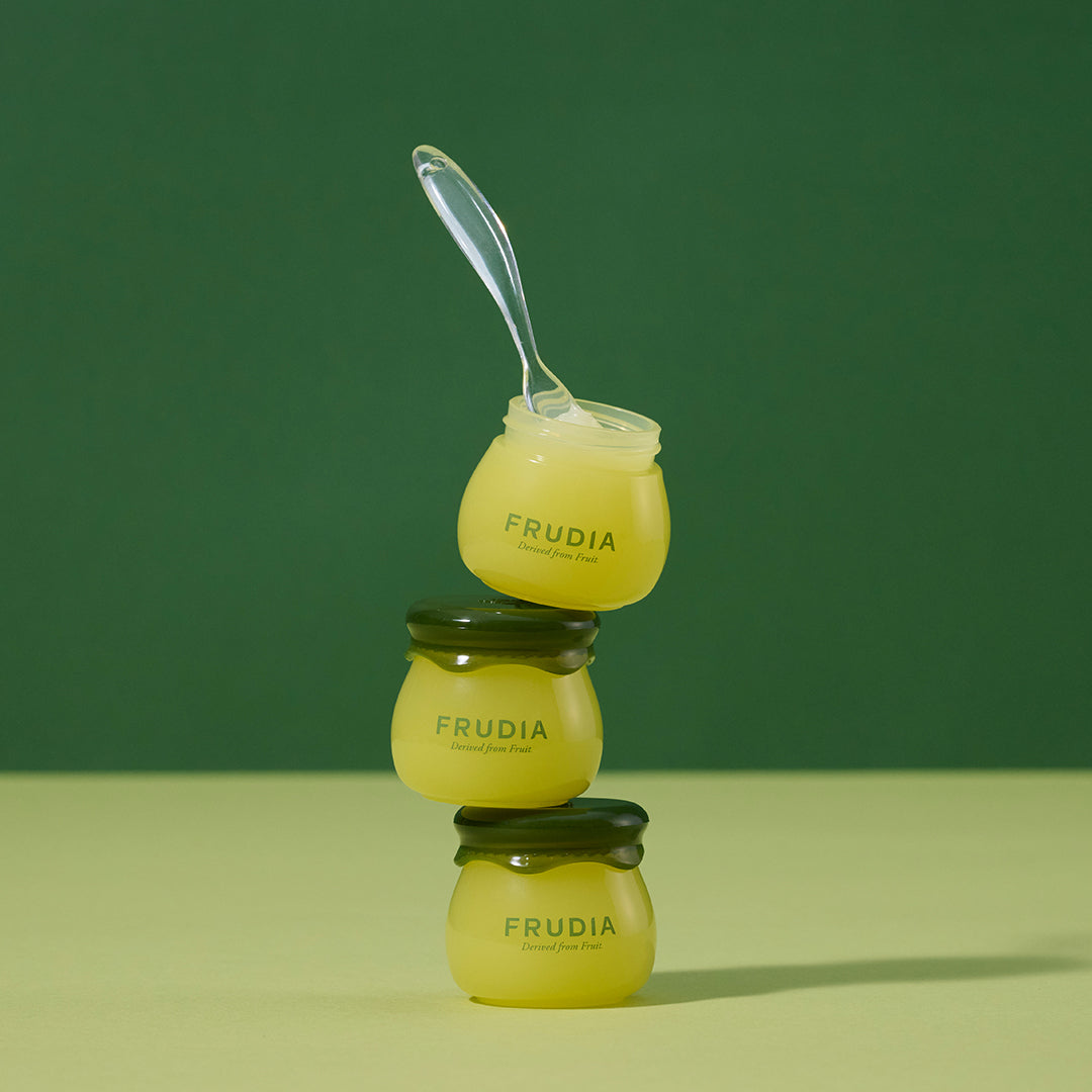 Stacked jars of Frudia skincare product with spoon on green background.