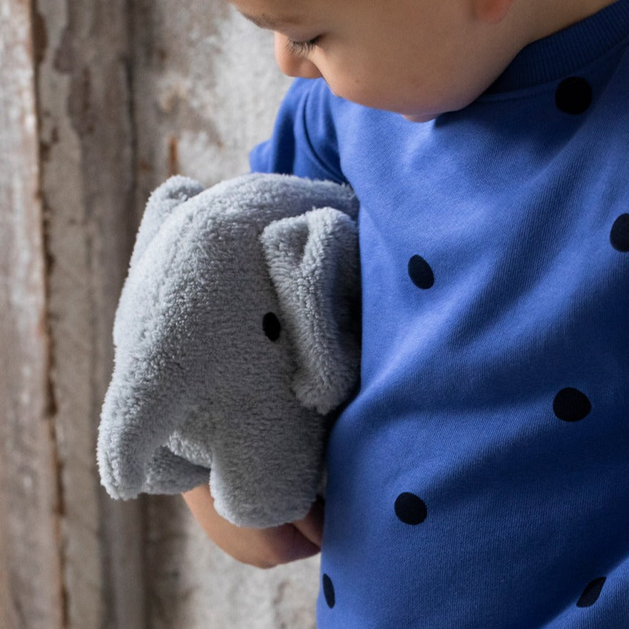 A child in a blue polka dot shirt holds a gray plush elephant.