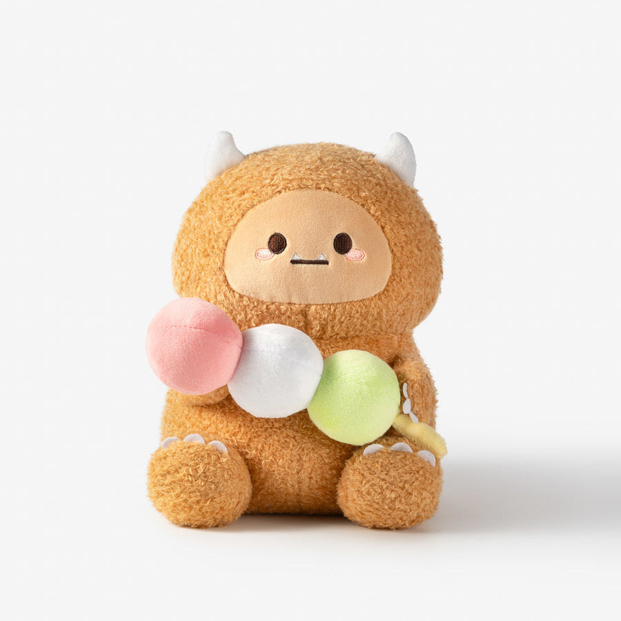 A plush toy character with a fuzzy tan body, small white horns, and a simple face, holding three soft balls in pink, white, and light green, photographed on a clean white background.