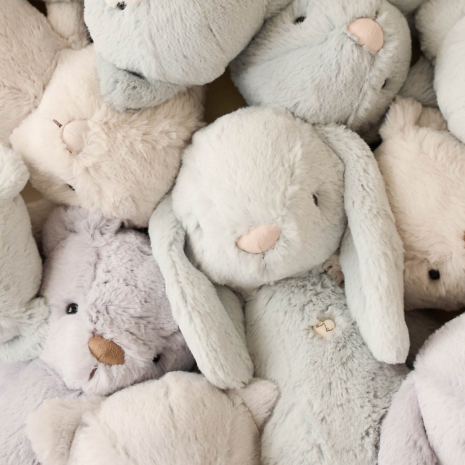 Pile of soft, plush toy animals in muted pastel colors.