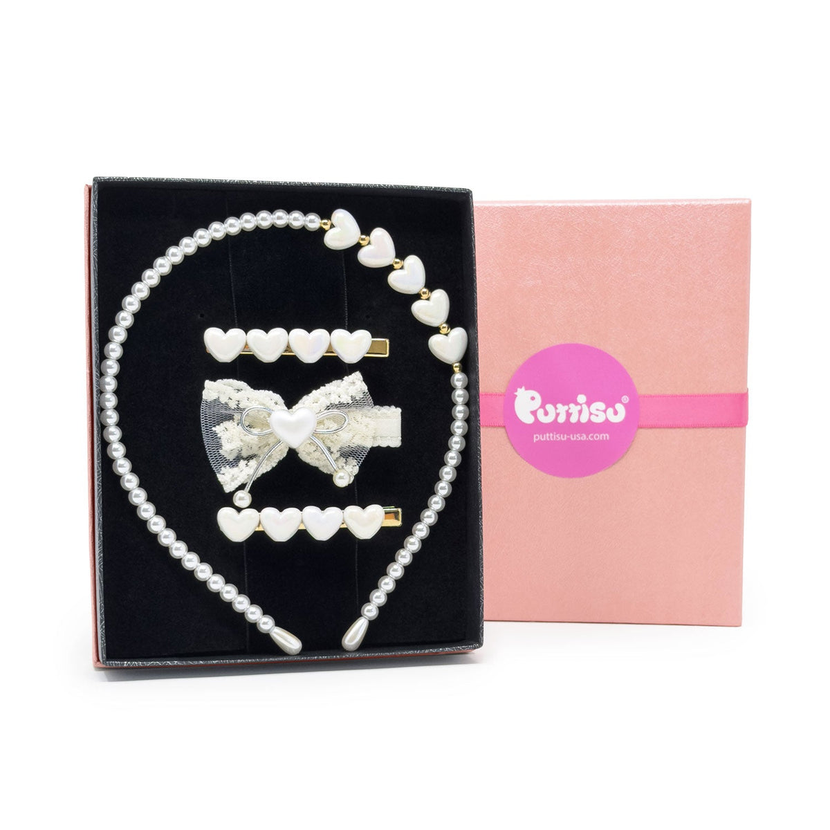 A pearl and white heart hair accessory set displayed in a black presentation box next to a pink gift box. The set includes a pearl headband with white heart accents, three white heart hair clips, and a white bow hair clip with a central white heart.