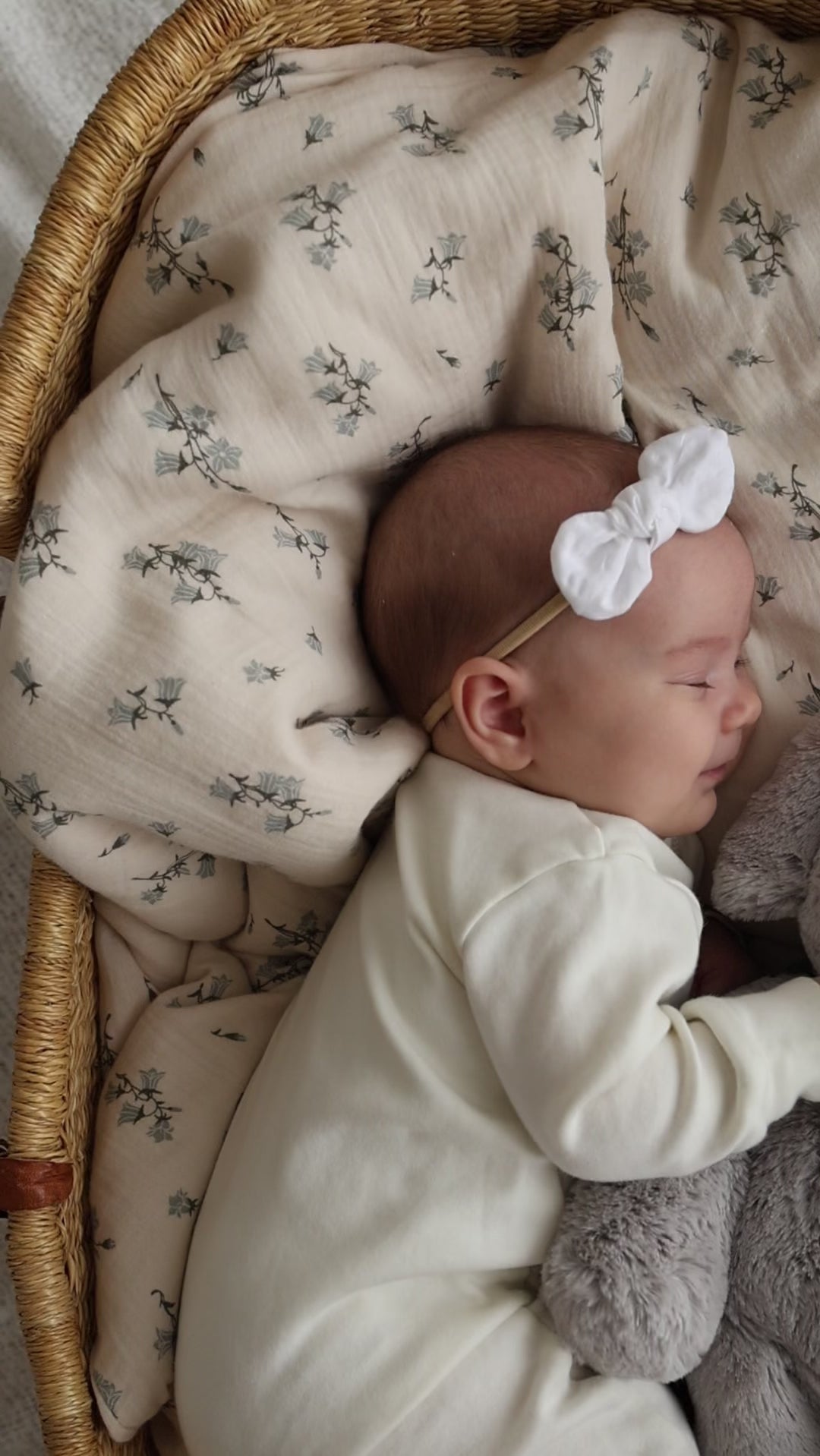 Sleeping baby in white onesie with bow headband in woven basket.