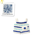 Crocheted white and blue doll clothes with a flower detail. A card featuring a blue flower design is visible in the top left.