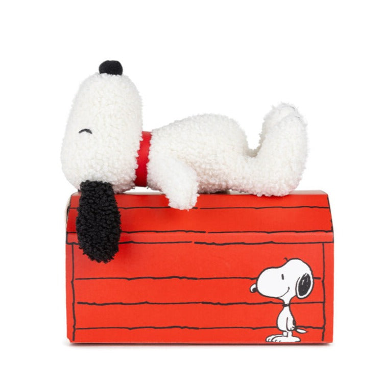 Stuffed Snoopy toy lying on a red dog house.