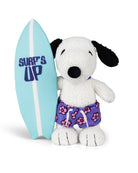 Stuffed Snoopy dog holding a surfboard and wearing flower-print swim trunks.