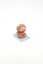 Brown cartoon character in meditation pose on a light blue square mat.