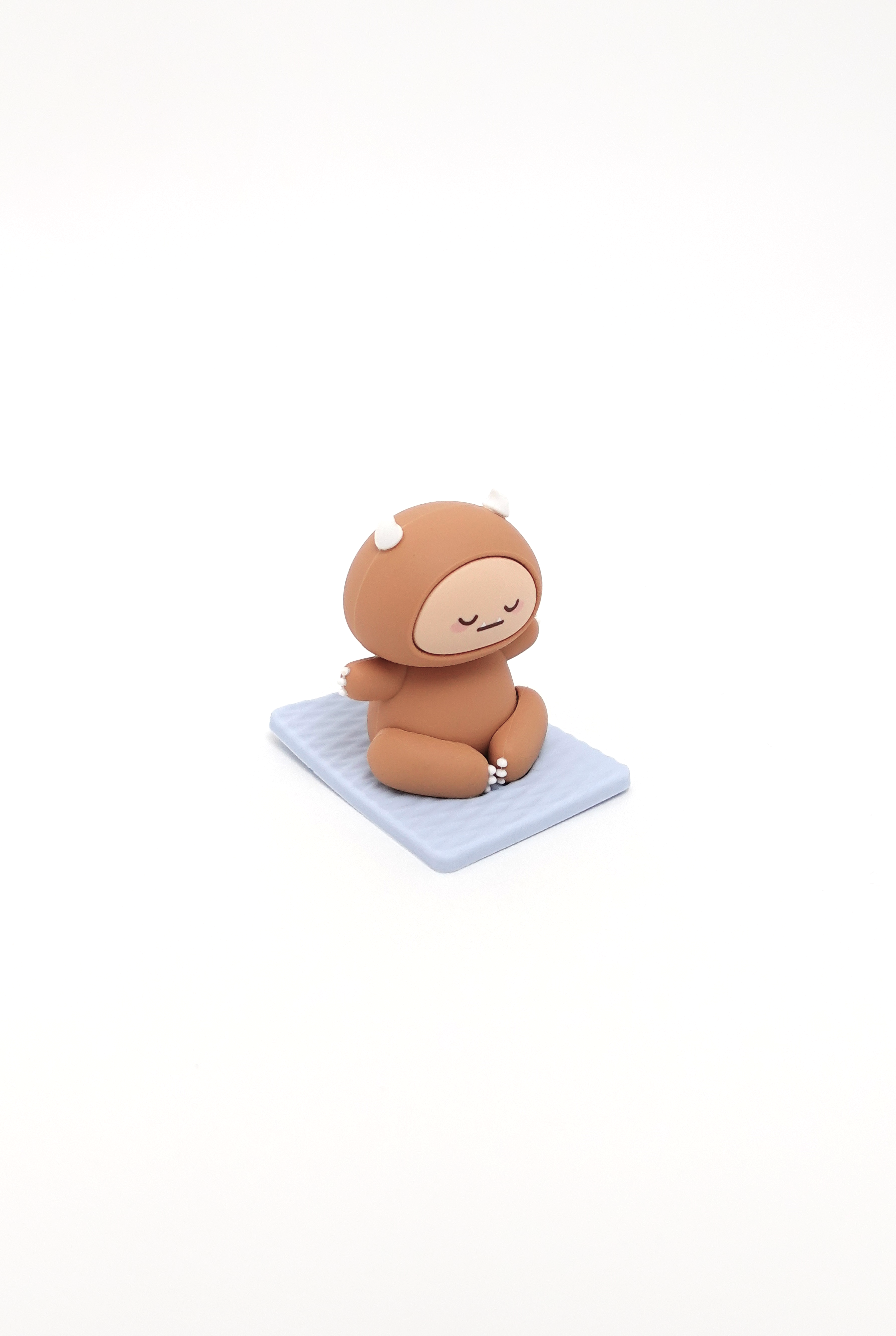 Brown cartoon character in meditation pose on a light blue square mat.