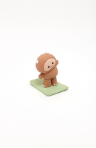 Brown cartoon figurine with white toes, claws, and horns on a green base.