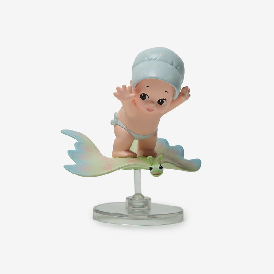 A collectible figurine of a baby mermaid riding a stingray on a clear plastic display stand, set against a plain light gray background.