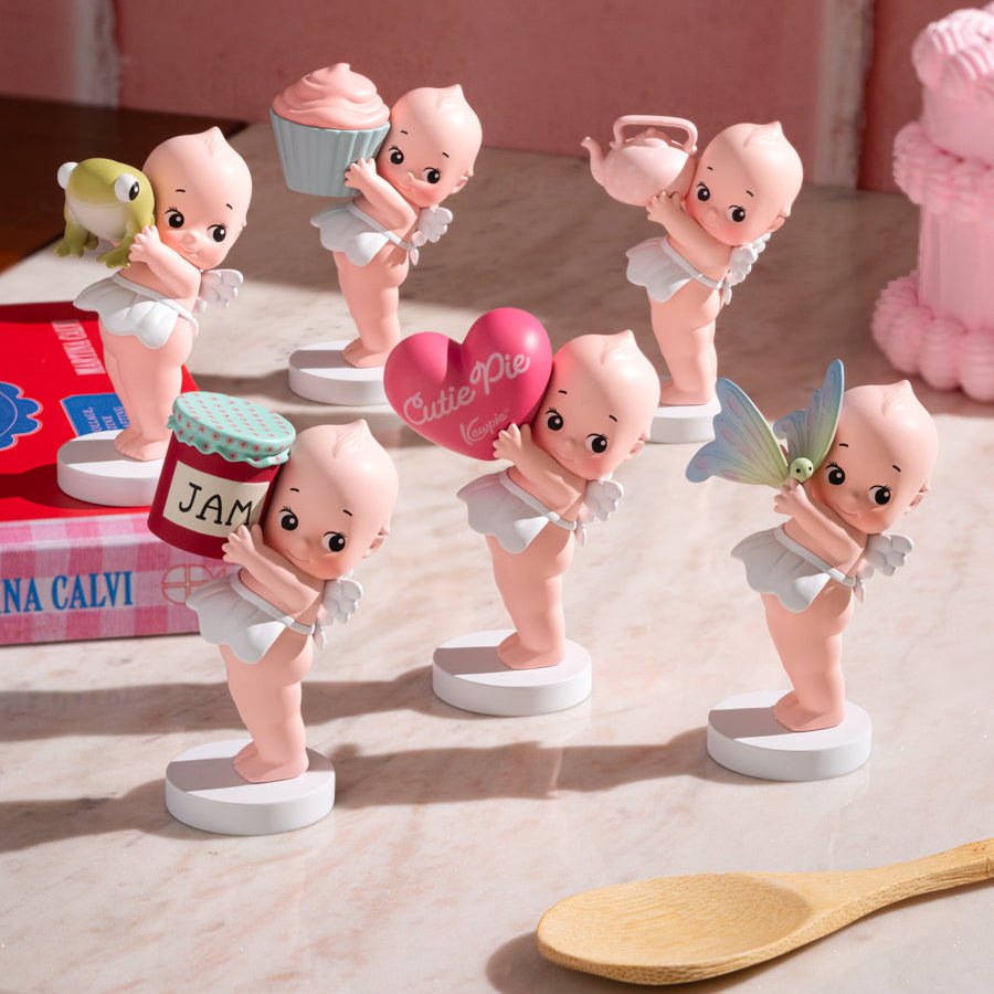 Set of baby-themed figurines on a wooden surface with a pink background