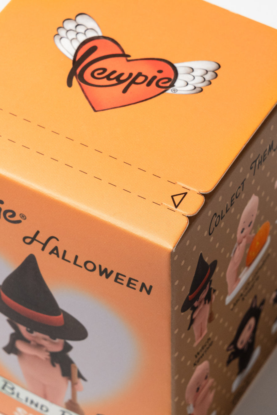 Close-up of an orange Kewpie Halloween blind box showing the Kewpie winged heart logo on top and Halloween-themed character illustrations on the sides.