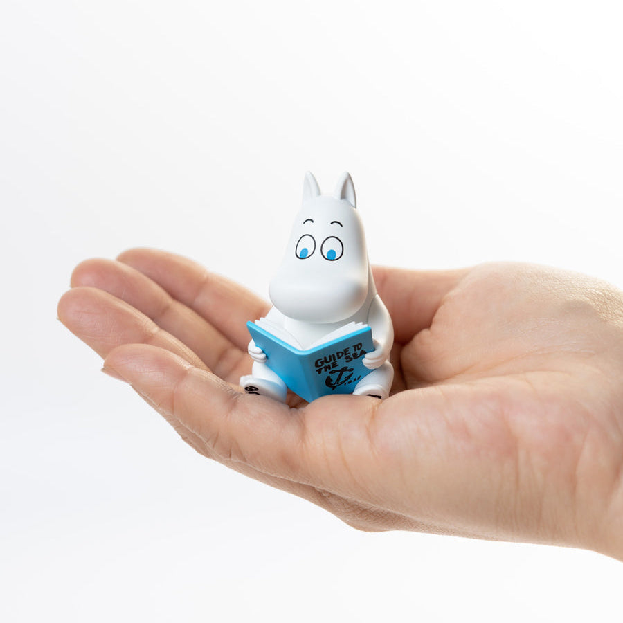 Small white figurine with blue book held in a hand against a white background
